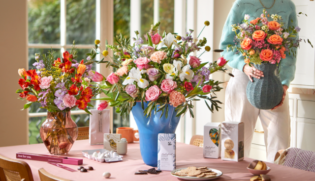 An image of a lady placing a vase full of flowers onto a table